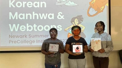 Three students in front of classroom, each holding a book
