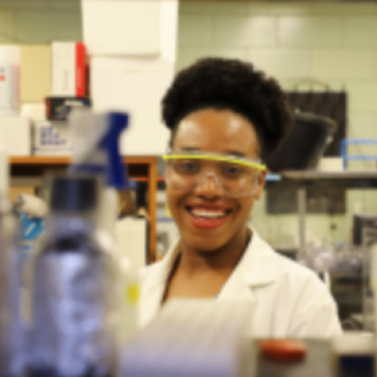 Student wearing safety goggles behind beakers in science lab.