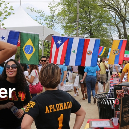 Large group of students enjoying involvement fair in front of various country flags.