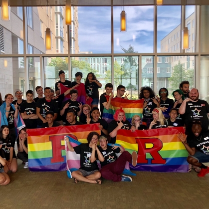 Large group of students pose with LGBTQ+ flags celebrating Q-MMUNITY event